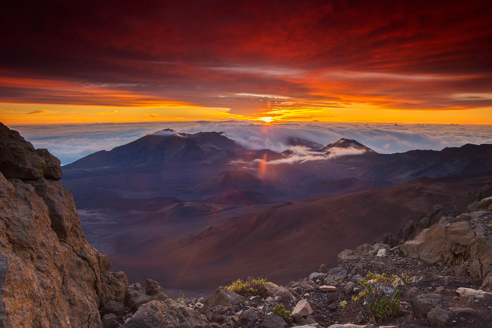 A sunset scene from a mountain top looking towards the setting sun with cloud coving lower mountains in the distance
